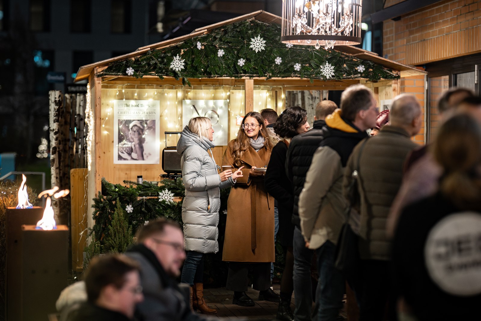 Weihnachtlich geschmückte Holzhütte mit Tannengrün, Gäste stossen an einer Weihnachtsfeier an